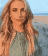 a woman is standing on a beach wearing a green dress and looking at the camera .