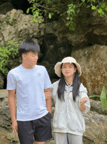 a girl wearing a hat stands next to a boy wearing a white shirt