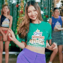 a woman in a green crop top that says our stories shine this christmas
