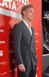 a man in a suit stands on a red carpet in front of a wall with the number 20 on it