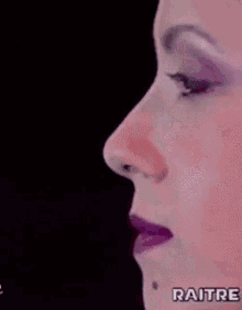 a close up of a woman 's face with purple lipstick and the word raitre in the corner .