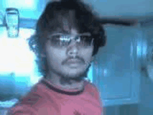 a man wearing sunglasses and a red shirt is standing in front of a window .