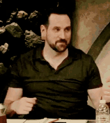 a man with a beard sits at a table with a bottle of water in front of him