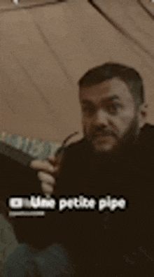 a man with a beard and mustache is sitting in a dark room holding a cigarette .