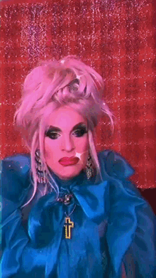 a drag queen is wearing a blue coat and a cross necklace
