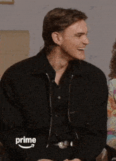 a man in a black jacket is laughing in front of a prime logo