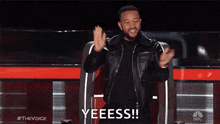 a man in a leather jacket is sitting in a chair on a stage applauding .
