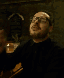 a man wearing glasses and a black shirt waves his hand