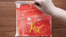 a person is painting a picture on a canvas with red and yellow paint