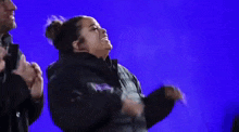 a woman is dancing in front of a blue background with a man clapping behind her