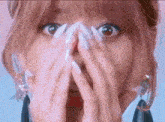 a close up of a woman with long white nails covering her face with her hands .