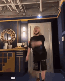a woman in a black shirt and shorts is dancing in a room with a mirror on the wall .