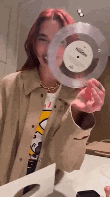 a woman is holding a record in front of her face and smiling .