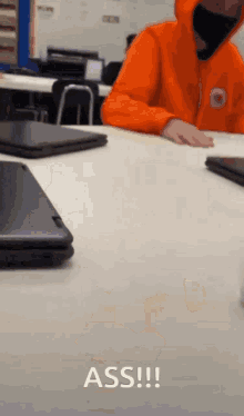 a person wearing an orange hoodie sits at a desk with a laptop and says " ass !!! "