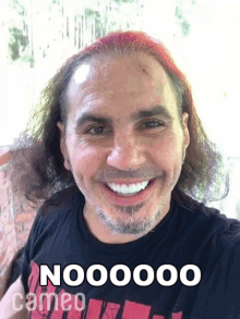 a man with red hair is smiling and wearing a black t-shirt that says nooooo cameo