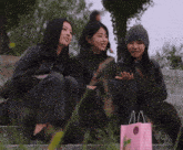 three women sit on a set of stairs with one holding a pink bag that says aa