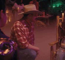 a man wearing a cowboy hat and a plaid shirt is sitting in a chair