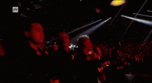a man in a blue jacket holds a microphone in front of a crowd with yle written on the bottom