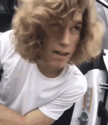 a man with blonde curly hair is wearing a white shirt and sitting in a boat .