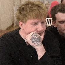 a man with a tattoo on his wrist is sitting at a table .