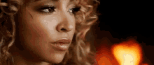 a close up of a woman 's face with curly hair and a fire in the background .