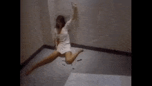 a woman in a white dress is jumping in the air on the floor .