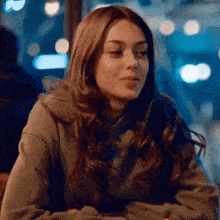 a woman in a hoodie is sitting at a table with her arms crossed and looking at the camera .