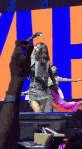 a woman in a black dress is dancing on a stage in front of a large screen with the letter h