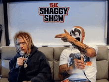 two men are sitting on a couch in front of a sign that says shaggy show