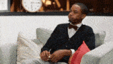 a man in a bow tie is sitting on a couch with a notebook in his hand .
