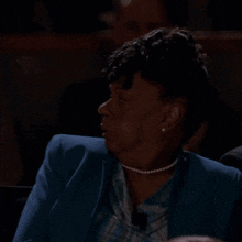 a woman in a blue jacket and pearl necklace is covering her face with her hand