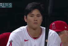 a baseball player wearing a red a hat sits in the dugout