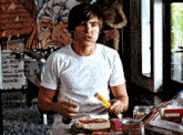 a man in a white t-shirt is eating a sandwich with a box of kix in his hand