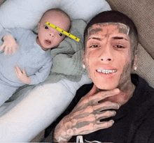a man with a tattoo on his face holds a baby with a tape measure on his forehead