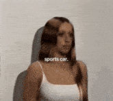 a woman in a white tank top is standing in front of a sports car advertisement