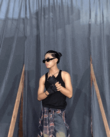 a man wearing sunglasses and a plaid shirt stands in front of a blue curtain