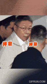 a man in a suit and tie is surrounded by other men with chinese writing on the bottom right