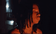 a woman with dreadlocks is standing in the dark with her eyes closed .