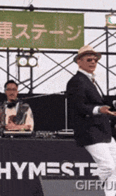 a man in a suit is dancing in front of a sign that says hymest