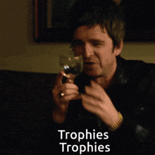 a man holding a glass of wine with the words trophies trophies written below him