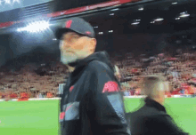 a man with a beard is walking on a soccer field wearing a nike jacket