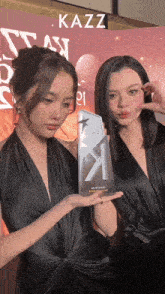 two women holding a trophy with the word kazz on the bottom right