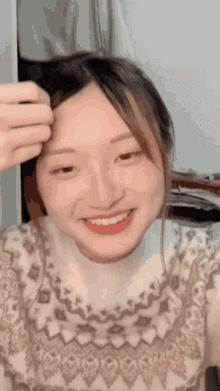 a woman wearing a sweater is smiling and touching her hair