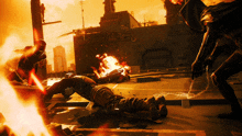 a man is laying on the ground in front of a building with a fire behind him