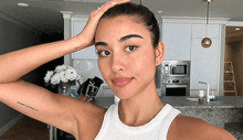 a woman with a tattoo on her arm is standing in a kitchen holding her head .