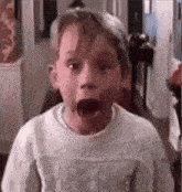 a young boy in a sweater is making a surprised face .