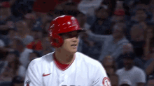 a baseball player wearing a red helmet is standing in front of a crowd of people .
