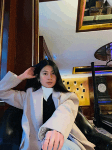 a woman in a white coat sits in a room with a clock on the wall