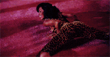 a woman in a leopard print jumpsuit is laying on a pink carpet