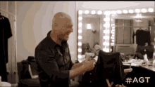 a bald man is sitting in a chair in front of a mirror in a dressing room .